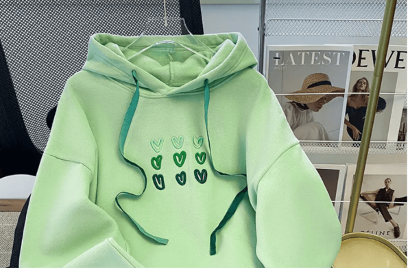 An image of a cozy green sweatshirt with custom embroidery on the chest. The embroidery features a vibrant, colorful small heart design, adding a unique and personal touch to the garment.