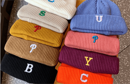 Custom embroidered beanies in various colors, each with a different letter embroidered on the front. The letters are designed in different vibrant colors, adding a pop of color to the cozy knit beanies. The custom embroidery gives the beanies a unique and personalized touch, making them a stylish accessory for any cold-weather outfit.